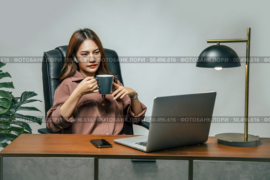 Portrait of smiling happy beautiful asian woman relaxing with hot coffee, She using technology of laptop computer to working from home during self-isolation and quarantine covid-19 coronavirus outbreak. Стоковое фото, агентство Ingram Publishing / Фотобанк Лори