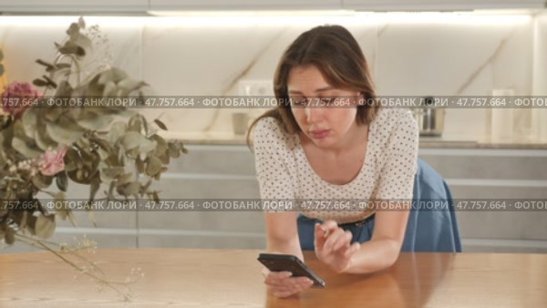 Portrait of upset frustrated young woman standing in home kitchen, looking at smartphone, waiting for message. Стоковое видео, видеограф Яков Филимонов / Фотобанк Лори