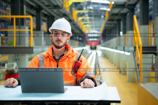 Portrait of Young male technician sitting on the table in skytrain repair station, Check the details of the electric train repair in laptop. Стоковое фото, агентство Ingram Publishing / Фотобанк Лори