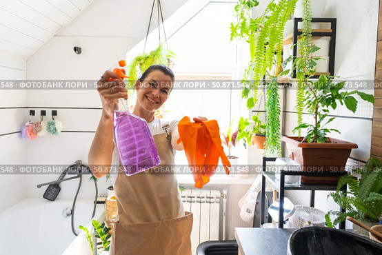 Portrait Woman in rubber gloves and apron manually cleaning in bathroom with rag cleaner and mop inside interior with home plants. Restoring order and cleanliness, cleaning servise. Стоковое фото, фотограф Ольга Симонова / Фотобанк Лори