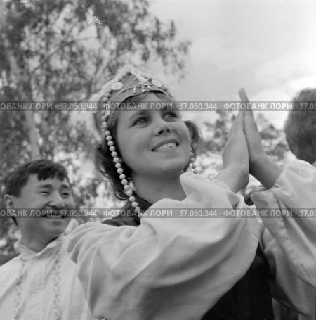 Портрет красивой девушки хлопающий в ладоши, молодая женщина участница творческого коллектива в сценической одежды для выступлений стоит на улице, Якутия, 1965. Редакционное фото, фотограф Варфоломей Тетерин / Фотобанк Лори