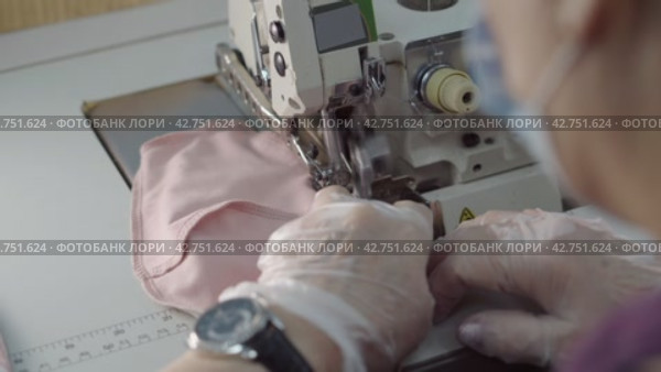 Пошив швейных изделий. Close-up female hands in protective gloves manufacturing medical face mask using a sewing machine. Стоковое видео, видеограф EStarodubov / Фотобанк Лори