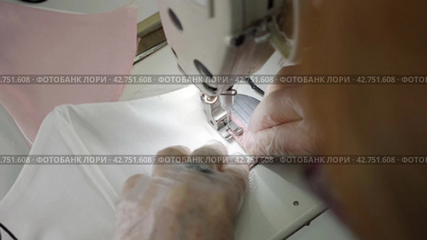 Пошив швейных изделий. Sewing of protective face masks during the coronavirus infection. Close-up female hands in protective gloves sew a medical mask on a sewing machine. Стоковое видео, видеограф EStarodubov / Фотобанк Лори