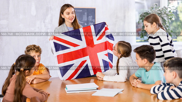Positive female teacher discussing with preteens students state flag of Great Britain in auditory of middle school. Стоковое фото, фотограф Яков Филимонов / Фотобанк Лори