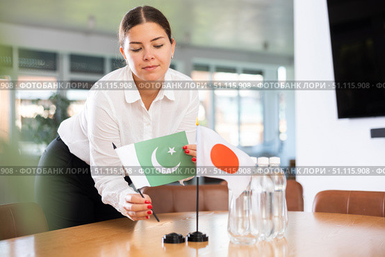 Positive young woman putting little flag of Pakistan on table next to the flag of Japan. Стоковое фото, фотограф Яков Филимонов / Фотобанк Лори