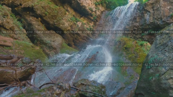 Поток чистой воды течет по скалам, рядом с бревнами. Вид снизу на водопад, падающий со скалы. Движение камеры снизу вверх. Красота дикой природы. Стоковое видео, видеограф Воловодов Владимир / Фотобанк Лори