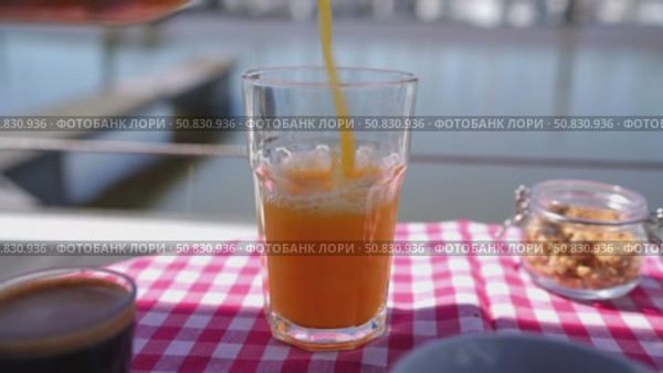 Pouring orange juice into glass on checkered tablecloth near lake. Стоковое видео, видеограф Данил Руденко / Фотобанк Лори