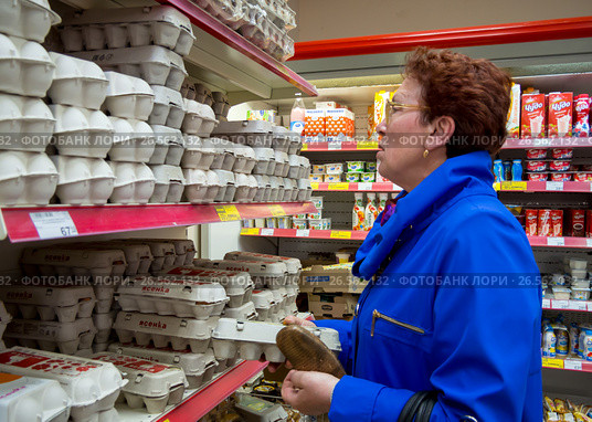 Пожилая женщина стоит у полок с куриными яйцами в продуктовом магазине (2017 год). Редакционное фото, фотограф Вячеслав Палес / Фотобанк Лори