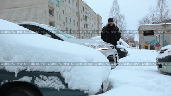 Пожилой водитель осматривает автомобиль, прогревающийся на зимней стоянке во дворе дома. Стоковое видео, видеограф Кекяляйнен Андрей / Фотобанк Лори