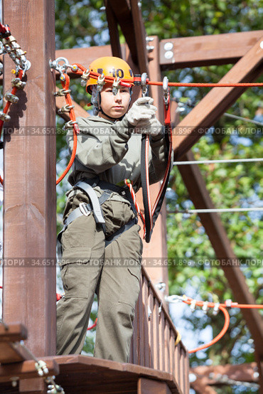 Preteen Caucasian girl climbs on rope course wearing climbing equipment. Стоковое фото, фотограф Кекяляйнен Андрей / Фотобанк Лори