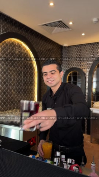 Professional bartender in black apron pours drink from shaker into glass.Male bartender pouring alcohol in glass, A young bartender making luxury cocktail. Редакционное видео, видеограф Zita Khasanova / Фотобанк Лори