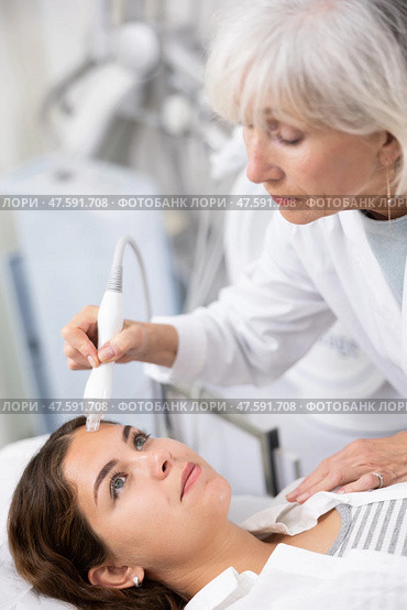 Professional mature female cosmetologist doing needleless high frequency mesotherapy in spa center. Non-invasive skin rejuvenation procedure. Стоковое фото, фотограф Яков Филимонов / Фотобанк Лори