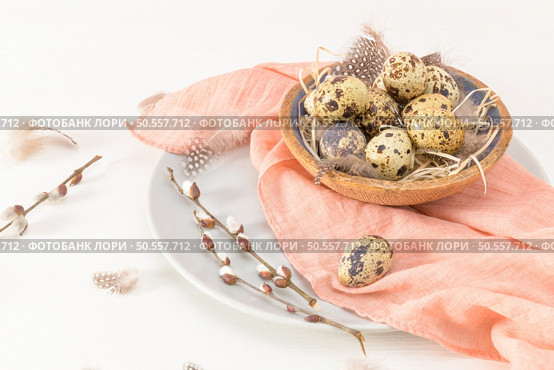 Quail eggs in a ceramic bowl with a peach fuzz pink colored scarf and bird feathers. Wooden table painted white. Background with elements suggestive of the Easter season. Стоковое фото, агентство Ingram Publishing / Фотобанк Лори