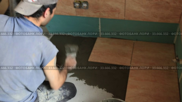 Рабочий плиточник укладывает керамическую плитку на пол. Стоковое видео, видеограф Евгений Ткачёв / Фотобанк Лори