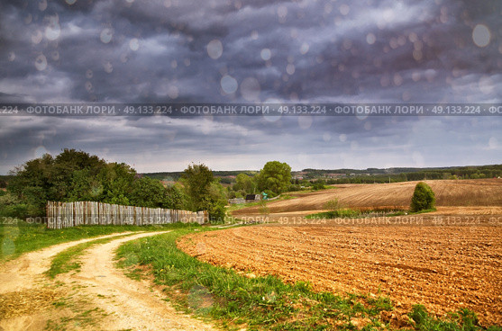 Rain and spring storm clouds above country road. Village and arable land field in spring. Стоковое фото, агентство Ingram Publishing / Фотобанк Лори
