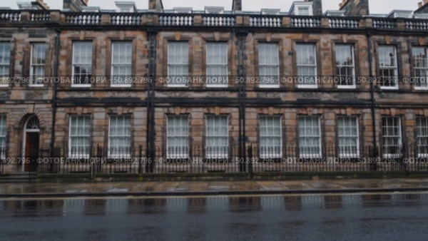 Rainwater glistening on cobblestone street, historic Georgian architecture in Edinburgh, dark stone walls framing white windows under overcast skies. Стоковое AI-видео, аниматор Данил Руденко / Фотобанк Лори