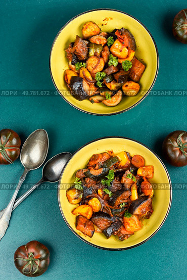 Ratatouille or stewed potatoes, eggplants, zucchini, onions, carrots in spicy sauce with greens.. Delicious vegetable stew in a bowl on the table. Стоковое фото, агентство Ingram Publishing / Фотобанк Лори