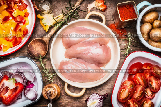 Raw chicken breasts , colorful cut vegetables in bowls , flavoring and cooking spoon. Preparation on rustic wooden background, top view. Стоковое фото, агентство Ingram Publishing / Фотобанк Лори