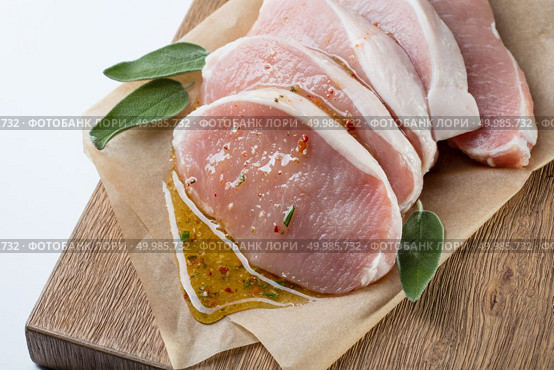 Raw meat. Pork escalope with sause made of honey and herbs with green sage leaves on wooden board against white background. Top view. raw pork escalope with sause made of honey and herbs. Стоковое фото, агентство Ingram Publishing / Фотобанк Лори