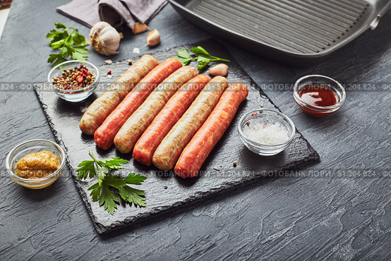 Raw meat sausages on a slate board, with herbs and spices and a square grill pan. View from above. Стоковое фото, фотограф Ирина Буракова / Фотобанк Лори