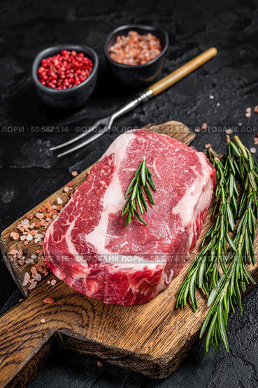 Raw Rib-eye Steak, beef marbled meat on wooden board with rosemary. Black background. Top view. Стоковое фото, агентство Ingram Publishing / Фотобанк Лори