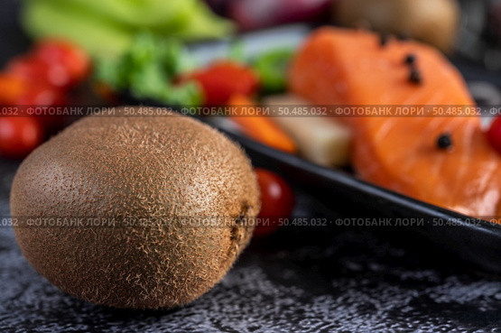 Raw salmon fillets, pepper, kiwi, pineapples, and rosemary onto a plate and black cement floor.Selective focus kiwi. Стоковое фото, агентство Ingram Publishing / Фотобанк Лори