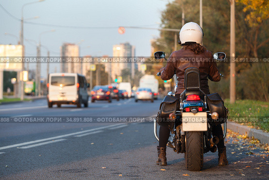 Rear view at motorcyclist with bike standing on urban road, female rider is ready to start movement in city. Стоковое фото, фотограф Кекяляйнен Андрей / Фотобанк Лори