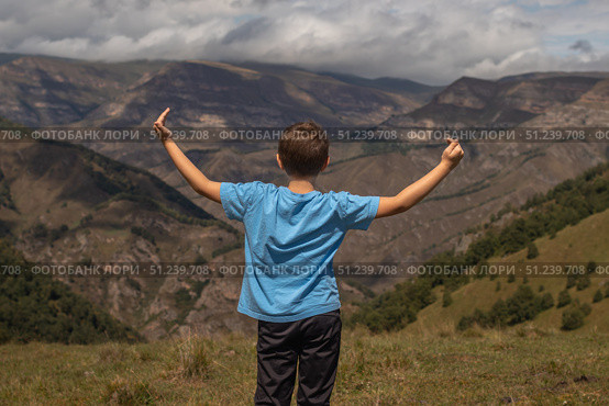 Rear view of boy standing with arms raised against mountains and dramatic clouds in the sky. Стоковое фото, фотограф Михаил Яковлев / Фотобанк Лори