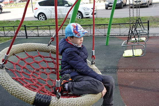 Ребёнок скучает на качелях-корзине на детской площадке. The child is bored on the basket swing at the playground. (2024 год). Редакционное фото, фотограф Юрий Пуликов / Фотобанк Лори