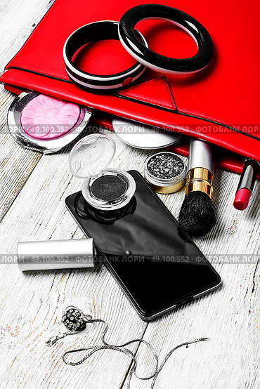 Red clutch bag and ladies accessories. Fashionable ladies handbag with cosmetics and phone on light background. Стоковое фото, агентство Ingram Publishing / Фотобанк Лори