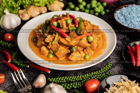 Red curry with pork in a white plate with spices on black cement. Стоковое фото, агентство Ingram Publishing / Фотобанк Лори