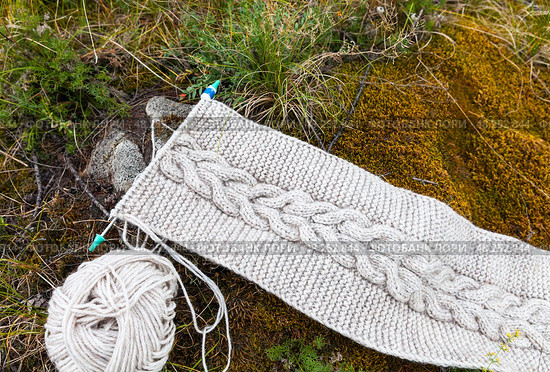 Relaxation in forest park and knitting in nature. Top view of handmade knitted warm scarf with braid made of natural wool yarn against soft green moss and grass in forest. DIY concept. Close-up, top view. Стоковое фото, фотограф Виктория Катьянова / Фотобанк Лори