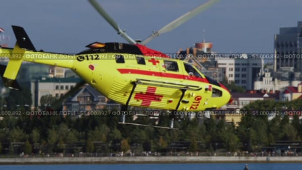 Rescue medical helicopter with yellow and red colors is flying low above river in urban area. It responds to emergency in difficult-to-access location. Стоковое видео, видеограф Strunov David / Фотобанк Лори