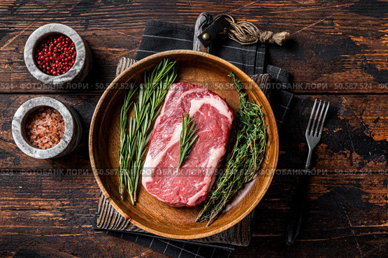 Rib-eye raw Steak, rib eye beef marbled meat in wooden plate with rosemary and thyme. Wooden background. Top view. Стоковое фото, агентство Ingram Publishing / Фотобанк Лори