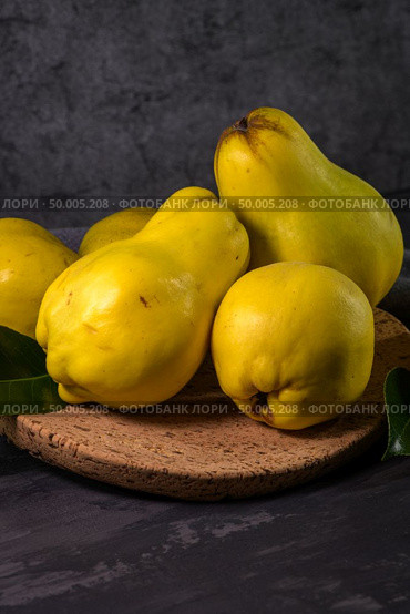 Ripe yellow quinces or queen apple fruits and sliced quince halves with seeds in craft cork plates on black rustic background. Стоковое фото, агентство Ingram Publishing / Фотобанк Лори