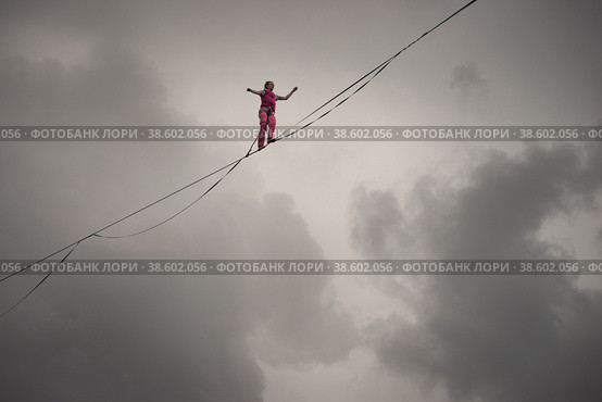 Rocks of a Triangular lake, Russia - August 2, 2021: A rope-walker girl walks along the highline against the background of a dramatic sky. Редакционное фото, фотограф Happyphotons / Фотобанк Лори