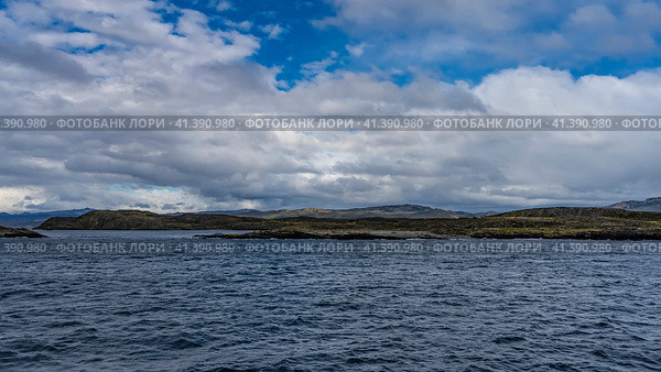 Rocky islets with sparse stunted vegetation are visible in the Beagle Channel. A mountain range against a background of blue sky and clouds in the distance. Ripples on the water. Argentina. Tierra del Fuego Archipelago. Стоковое фото, фотограф Вера Ивановна Кубарева / Фотобанк Лори