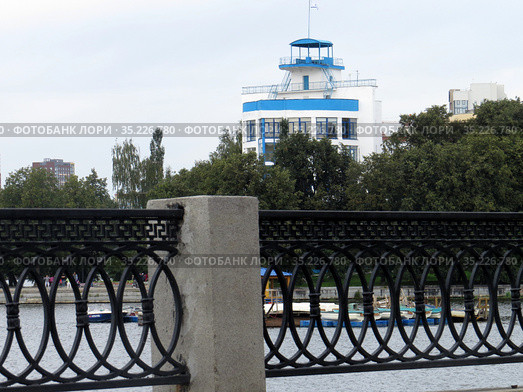 Россия. Екатеринбург. Набережная городского пруда, фрагмент ограды. Вдали здание-кораблик стадиона "Динамо" (2019 год). Стоковое фото, фотограф Владислав Сабанин / Фотобанк Лори