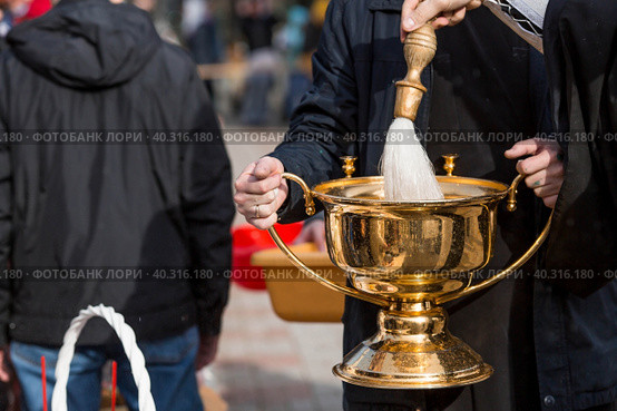 Russia, the City of Vidnoye, April 15, 2023. Easter service. The priest sprinkles people and Easter treats with holy water at the entrance to the temple. People go to sanctify eggs and cakes. Стоковое фото, фотограф Photojuli / Фотобанк Лори