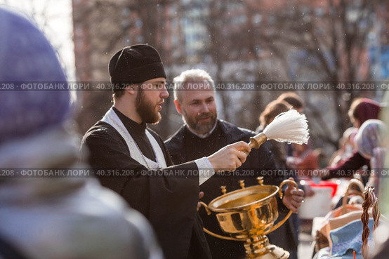 Russia, the City of Vidnoye, April 15, 2023. Easter service. The priest sprinkles people and Easter treats with holy water at the entrance to the temple. People go to sanctify eggs and cakes. Редакционное фото, фотограф Photojuli / Фотобанк Лори