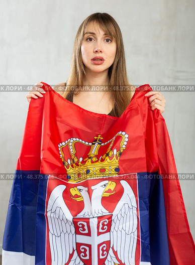 Sad young woman holding flag of Serbia against unicoloured background. Стоковое фото, фотограф Яков Филимонов / Фотобанк Лори