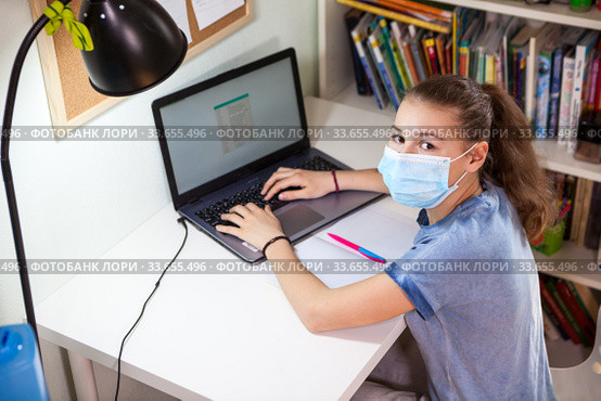 Schoolgirl working on laptop while sitting at home, child wearing medical mask suring self-isolation. Стоковое фото, фотограф Кекяляйнен Андрей / Фотобанк Лори