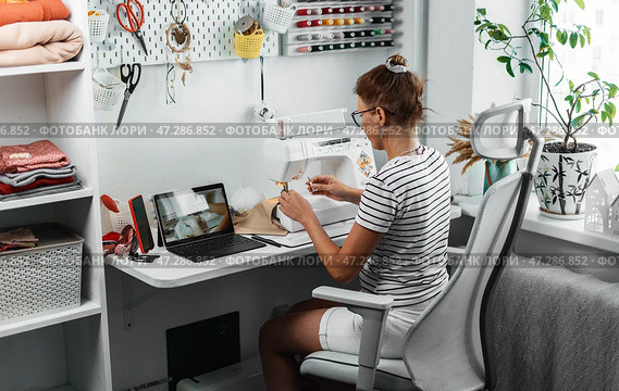 Seamstress enjoys working in well-organized sewing studio, surrounded by tools and materials. Comfortable environment enhances creativity and productivity in tailoring business. Стоковое фото, фотограф Енваев Андрей / Фотобанк Лори