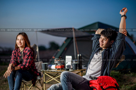 Selective focus Handsom man sitting on chair and streching arms near his girlfriend at front of camping tent, They are smile with happiness and freshness when relaxing in nature. Стоковое фото, агентство Ingram Publishing / Фотобанк Лори