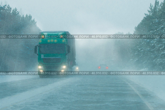 Semi-trailer truck at the interurban road during a heavy blizzard. Cars and truck drive on the road in a snow storm in the evening. Стоковое фото, фотограф Трегубов Николай / Фотобанк Лори