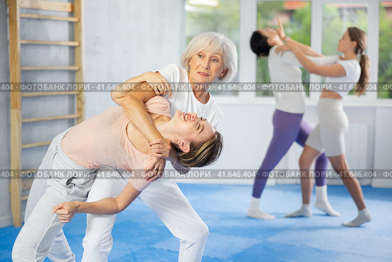 Senior woman applying inverted headlock during mock bout in self-defense training. Стоковое фото, фотограф Яков Филимонов / Фотобанк Лори