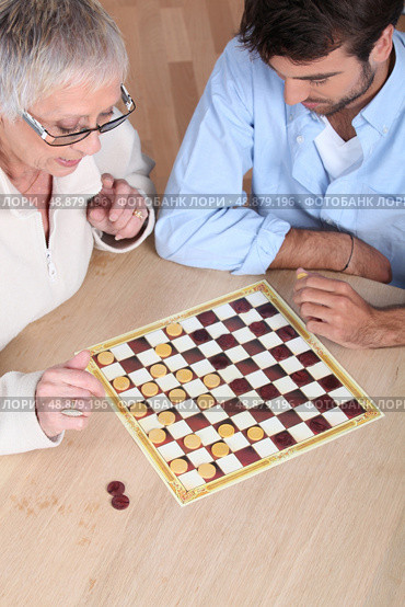 Senior woman playing checkers with a young man. Стоковое фото, агентство Ingram Publishing / Фотобанк Лори