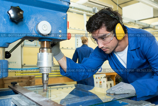 serious trainees focused on drilling metal piece with professional machinery. Стоковое фото, агентство Ingram Publishing / Фотобанк Лори