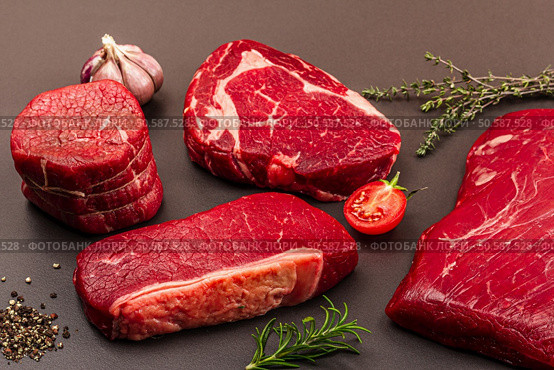 Set of various steaks with classic spices and herbs. Fresh raw meat cuts includes ribeye, eye round, flank and striploin steaks. Black stone concrete background, flat lay, close up. Стоковое фото, агентство Ingram Publishing / Фотобанк Лори