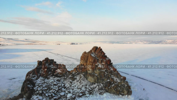 Shamanka Rock or Cape Burkhan on a sunny winter day. Frozen Lake Baikal, covered with snow. Olkhon Island. Скала Шаманка или мыс Бурхан в солнечный зимний день. Замерзшее озеро Байкал, покрытое снегом. Остров Ольхон. Стоковое видео, видеограф Виктория Тельминова / Фотобанк Лори